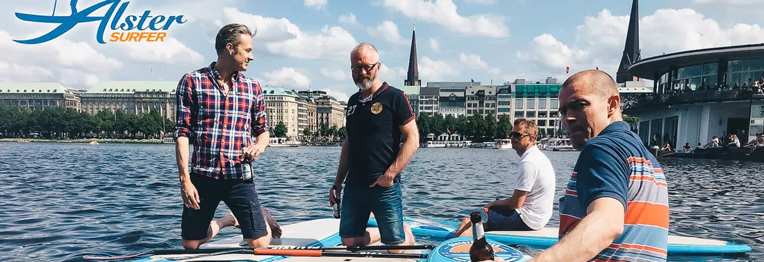 Eine Gruppe steht mit Boards auf der Alster, dahinter die Skyline